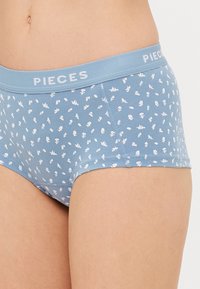 Svijetloplave ženske gaćice s malim bijelim cvjetnim uzorcima. Mekani materijal, elastična pojas označena "PIECES", i oblikovani dizajn.