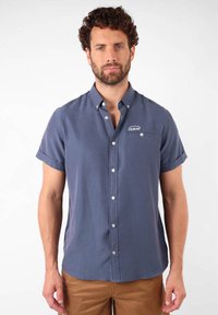 Chemise à manches courtes, à boutons, en tissu bleu marine, avec une poche poitrine ornée d'un logo et des manches retroussées. Design de col classique.