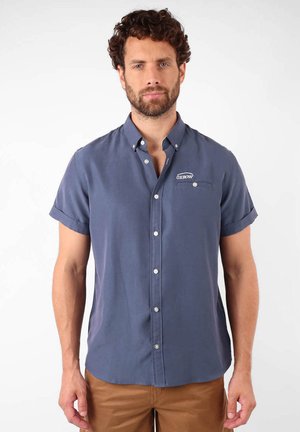 Chemise à manches courtes, à boutons, en tissu bleu marine, avec une poche poitrine ornée d'un logo et des manches retroussées. Design de col classique.