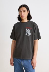 T-shirt en coton gris foncé à manches courtes, avec un imprimé graphique blanc et rouge d'un squelette sur une bicyclette, étiqueté "Finisher 1983."