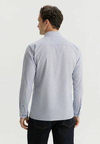 Męska koszula z długim rękawem w jasnoniebieskim kolorze z delikatnymi paskami, z kołnierzykiem rozłożonym, guzikami na mankietach i gładką teksturą. Ciemne dżinsy widoczne na wysokości talii.