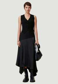 Top noir sans manches en rib et à boutons, associé à une jupe asymétrique noire fluide et des bottes noires hauteur genou. Inclut un sac à main noir.