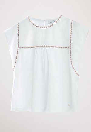 Blouse blanche à manches courtes avec encolure ronde et bordure marron festonnée le long du col, des épaules et du yoke de la poitrine, présentant un petit pli sous le yoke.