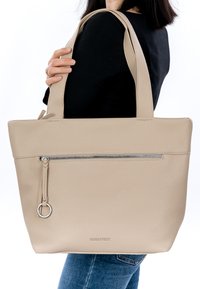 Naine musta toppi ja teksadega, üle õla kandmas suurt beeži nahast käekotti, millel on ees tõmblukk ja pikad sangad.