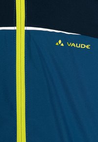 Blue jacket with a green zip, featuring a navy upper section, white accents, and the VAUDE logo in yellow. Smooth fabric texture.