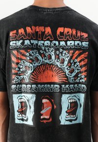 Črna bombažna majica s rdečim in modrim grafičnim potiskom. Oblikovanje vključuje kričeče ustnice, roke in besedilo "Santa Cruz Skateboards".