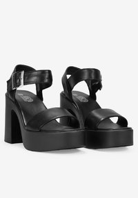 Tacones de plataforma negros con correas anchas, hebilla en el tobillo y textura mate. Presentan un tacón grueso y un diseño de punta abierta.