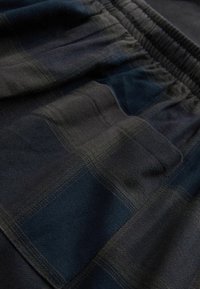 Tessuto a quadri neri e blu navy con una cintura elastica. Caratterizzato da una texture liscia e tasche laterali, che enfatizzano tonalità di colore attenuate.
