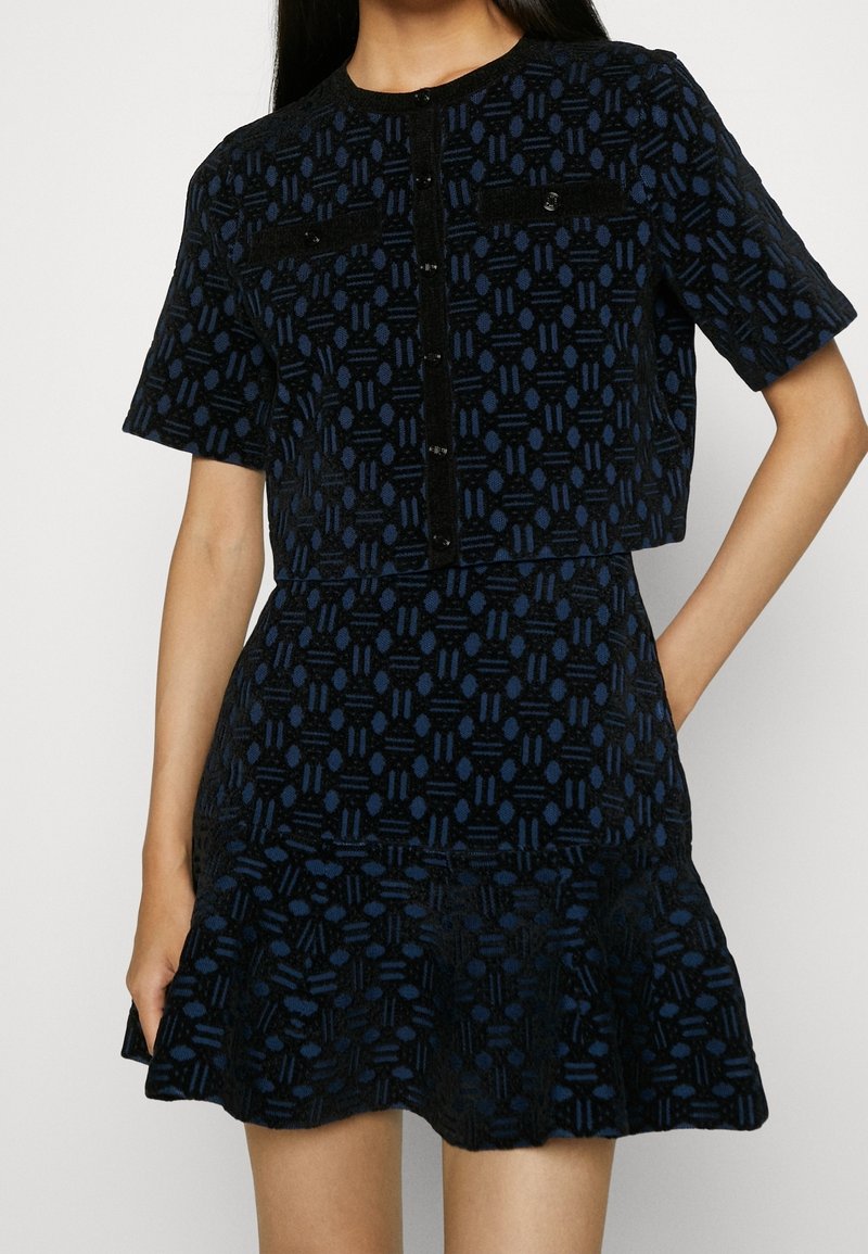 Femme portant un haut boutonné manches courtes à motif noir et marine associé à une jupe évasée taille haute assortie.