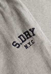 Szary bawełniany materiał z haftowanym napisem "S.DRY N.Y.C." w ciemnym granacie. Gładka tekstura o swobodnym designie i bez dodatkowych wzorów.