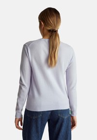 Svetle fialový svetr vyrobený z jemného materiálu, s dlouhými rukávy a žebrovaným lemem. V kombinaci s tmavě modrými džíny.