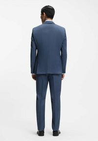 Dopasowany niebieski garnitur w prążki z pojedynczym rozcięciem, o wąskim kroju, z dopasowanymi spodniami, uzupełniony czarnymi butami.