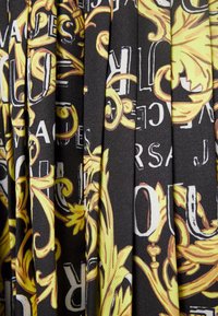 Svart tyg med en plisserad textur, prytt med ett livfullt gult barockmönster och vita textelement.