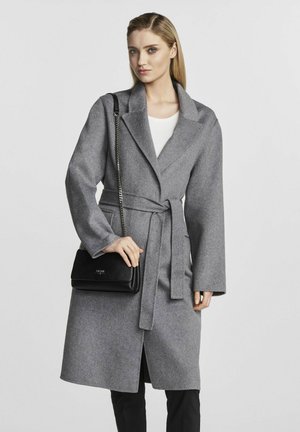 Szary wełniany płaszcz z szerokimi klapami, z paskiem w talii i długimi rękawami. W połączeniu z czarną torebką o teksturowanej powierzchni i białą bluzką. Prosty fason.