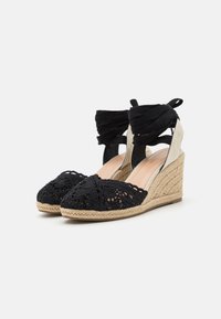 Black crocheted wedge heels with braided jute soles. Features thick black ankle straps and a rounded toe design.