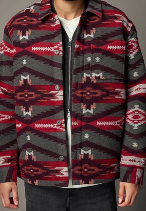 Wool jacket with a geometric red, gray, and black pattern. Features a button closure, chest pocket, and contrasting inner zip design.