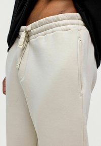 Lichtbeige joggers van zachte stof, met een elastische tailleband met trekkoord, zijzakken en een gladde textuur.