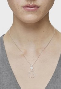 Collar de plata con un colgante en forma de oso acentuado con un corazón. El diseño de la cadena es delicado, con pequeños círculos interconectados.