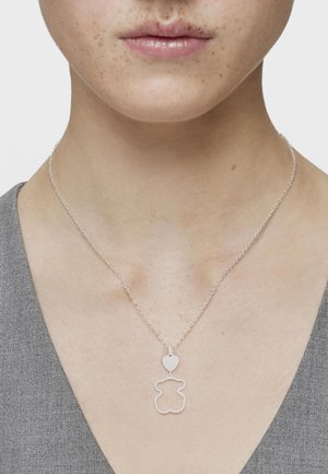 Collar de plata con un colgante en forma de oso acentuado con un corazón. El diseño de la cadena es delicado, con pequeños círculos interconectados.