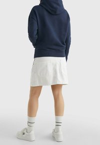 Felpa con cappuccio blu abbinata a una gonna di jeans bianca. La gonna presenta due tasche posteriori e una vestibilità casual e rilassata. Sneakers bianche e calze a righe.