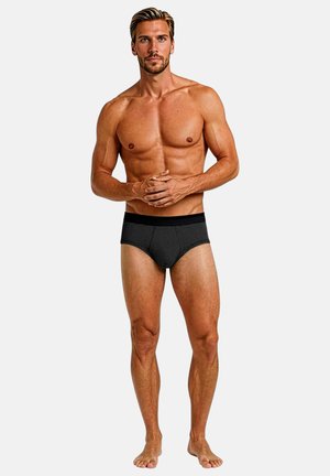 Schwarze und graue gestreifte Slips aus weichem Stoff. Eng anliegendes Design mit bequemem Bund. Modell posiert mit verschränkten Händen.