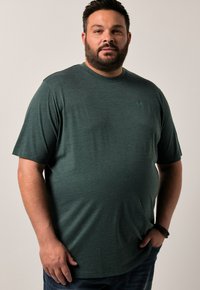 Tmavě zelené tričko s krátkým rukávem, kulatým výstřihem a jemnou texturou. Obsahuje malé logo na levé části hrudi. Měkká látka.