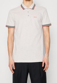 Polo gris clair en coton, avec une patte de boutonnage à trois boutons, un col rayé noir et rose, et le logo "BOSS" en rose sur la poitrine.