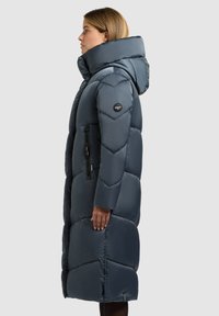 Sötétkék bélelt steppelt dzseki nagy kapucnival, steppelt mintával és cipzáras zsebekkel, sima, fényes felülettel.