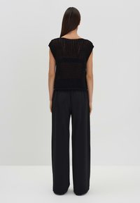 Mustat neulepusero, jossa on lyhyet hihat, rento istuvuus ja avoin kudontamalli, yhdistettynä leveälahkeisiin mustiin housuihin.