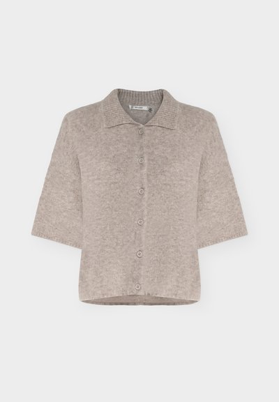 Cardigan beige à manches courtes avec boutons, texture douce et duveteuse et col plat, présenté sur fond uni.