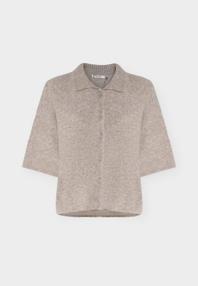 Cardigan beige à manches courtes avec boutons, texture douce et duveteuse et col plat, présenté sur fond uni.