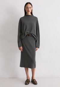 Pull en tricot gris avec un col montant, des manches longues et une coupe décontractée, associé à une jupe crayon assortie et une ceinture marron. Mocassins marron.