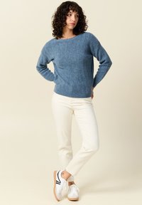 Maglione blu con texture, girocollo e maniche lunghe, abbinato a pantaloni bianchi a gamba affusolata e sneakers bianche con dettagli neri.