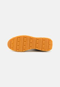 Suela de una zapatilla deportiva con un material de goma naranja, texturizada con patrones rectangulares y con una marca en relieve, sobre un fondo blanco.