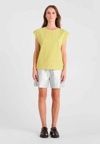 Geel en wit gestreept shirt met korte mouwen en een ontspannen pasvorm, gecombineerd met zilveren shorts en zwarte sandalen. Eenvoudig ontwerp, casual look.