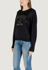 Schwarzer Strickpullover mit "Guess"-Logo und "Los Angeles"-Text aus Strasssteinen. Rundhalsausschnitt, lange Ärmel und geripptem Saum.