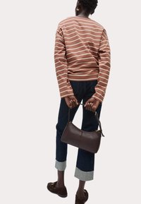 Bruine gestreepte longsleeve shirt, donkerblauwe cropped jeans met lichtgrijze manchetten, en een kleine bruine leren handtas met gouden hardware.