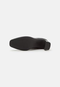 Schwarzer High Heel mit einem glatten Lederobermaterial, runder Spitze und einer strukturierten Gummisohle. Verfügt über einen stabilen Blockabsatz für mehr Stabilität.