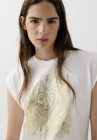 Hvid bomulds ærmeløs top med et stort guld skull og tværben print med en distressed tekstur, rund halsudskæring og afslappet pasform.