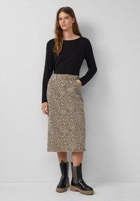 Jupe longue en imprimé léopard en coton avec une taille haute, dotée de poches latérales ; associée à un haut noir à manches longues et des bottines noires.