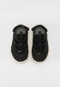 Μαύρα αθλητικά παπούτσια με λείο επάνω μέρος και τμήματα από πλέγμα, ρυθμιστική λωρίδα, ελαστικές κορδόνες και λευκή ελαστική σόλα.