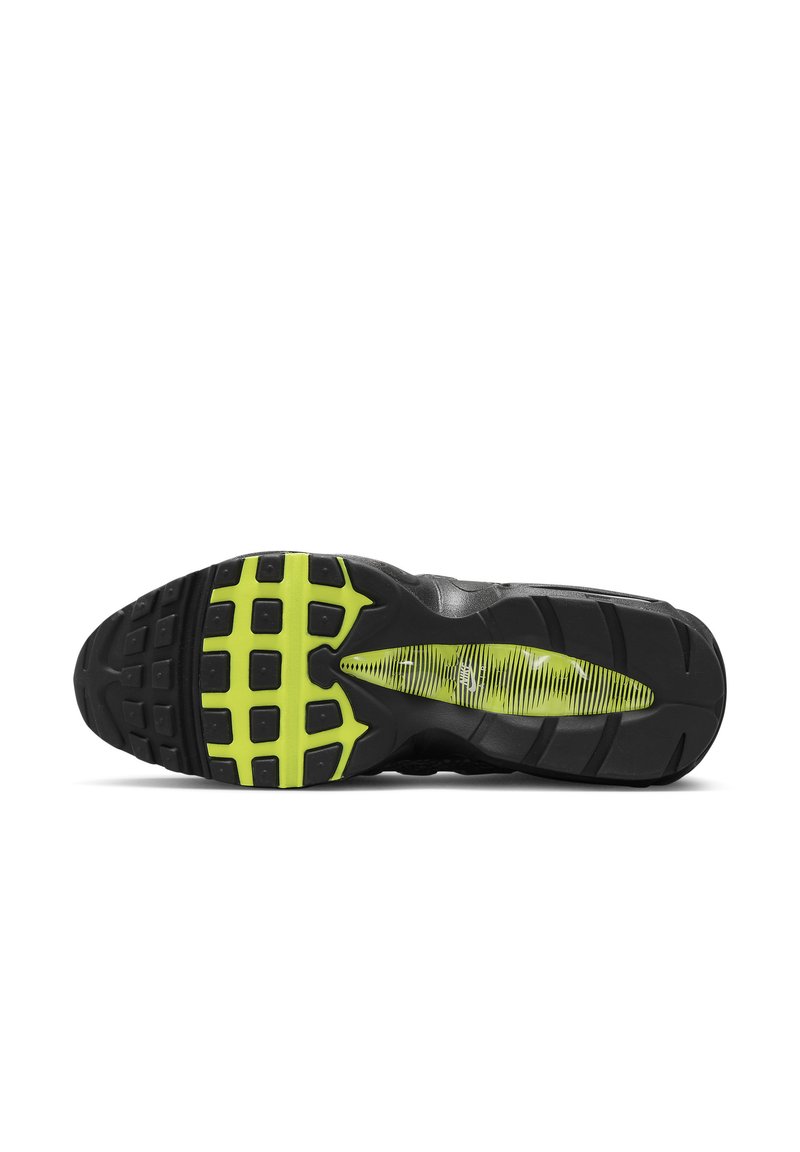 Suela de zapatilla deportiva negra con un patrón texturizado, que presenta acentos de goma amarilla y una sección de amortiguación de aire visible en el área del talón.