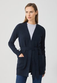 Námornícky pletený kardigán s dlhými rukávmi, rebrovanými manžetami, otvoreným predným dielom, viazacím pásom a dvoma prednými vreckami. Mäkká textúra, neformálny dizajn.