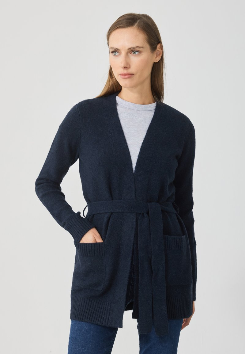 Námornícky pletený kardigán s dlhými rukávmi, rebrovanými manžetami, otvoreným predným dielom, viazacím pásom a dvoma prednými vreckami. Mäkká textúra, neformálny dizajn.