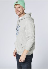 Gray cotton hoodie with a front pocket and blue graphic design. Paired with dark jeans and a light green ribbed beanie. Casual fit.