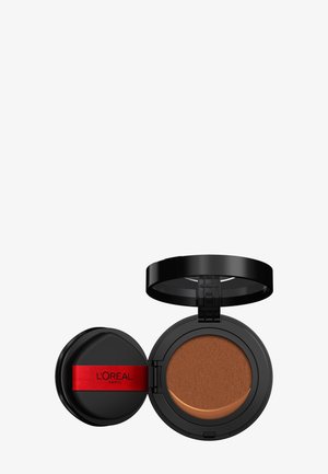 Boîtier compact noir de fond de teint ouvert montrant un fond de teint cushion marron moyen et un applicateur noir avec une bande rouge L'Oréal Paris.