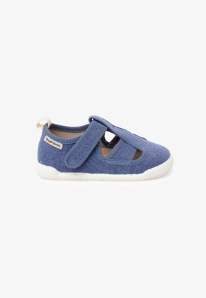 Chaussure en tissu bleu pour tout-petit avec bride réglable à scratch, semelle en caoutchouc blanche et étiquette sur le côté du talon.