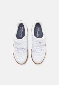 Λευκά δερμάτινα αθλητικά παπούτσια με υφασμάτινη υφή, διαθέτοντας ιμάντα με Velcro, σχέδιο με κορδόνια και σόλα από καουτσούκ γαύρου. Εμφάνιση του λογότυπου της Reebok.