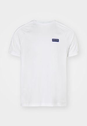 Balts īsām piedurknēm krekls ar raglanu piedurknēm, kuram ir zils taisnstūra logo kreisajā krūtī un maiga tekstūra uz auduma.