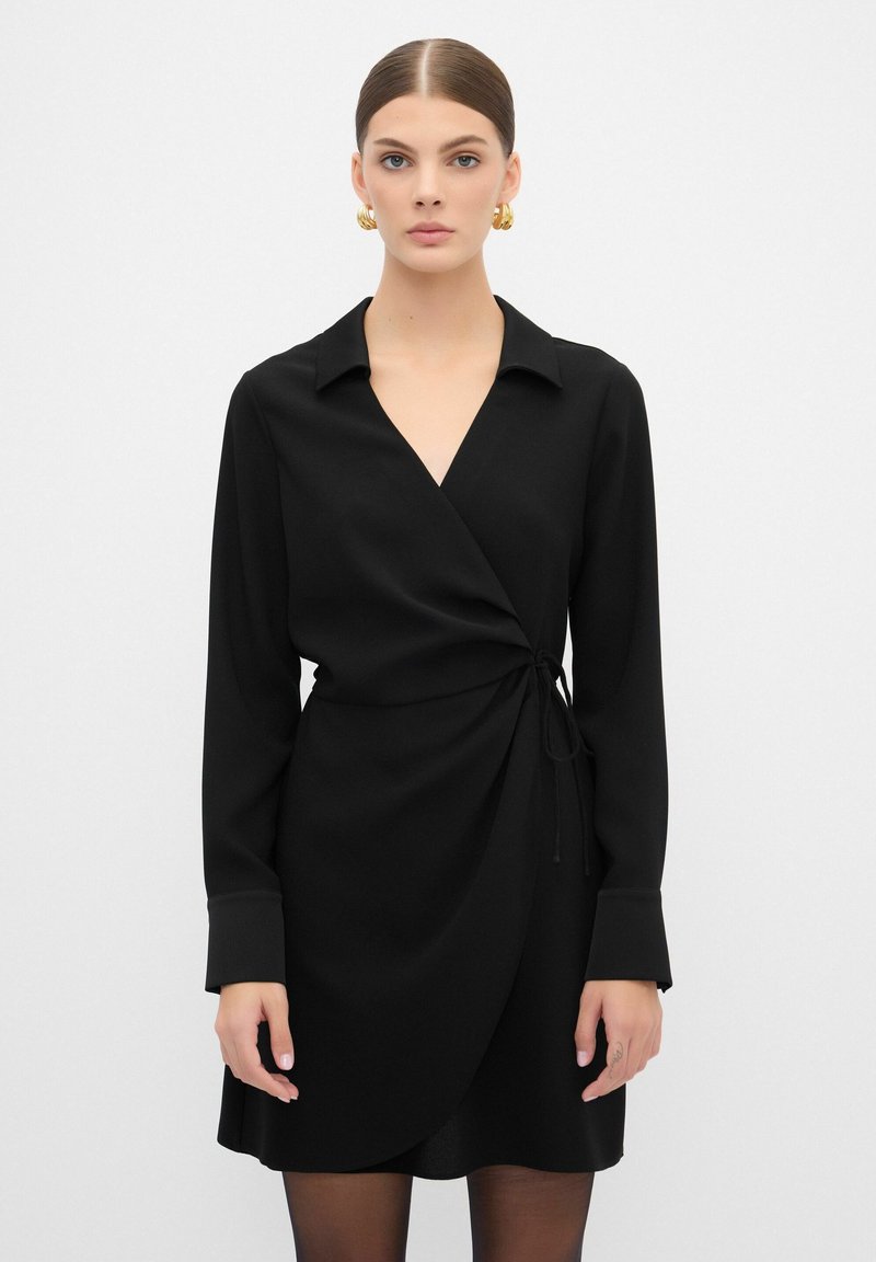 Vestito avvolgente nero con maniche lunghe, colletto e dettaglio legato regolabile in vita. Tessuto liscia con una silhouette affusolata.